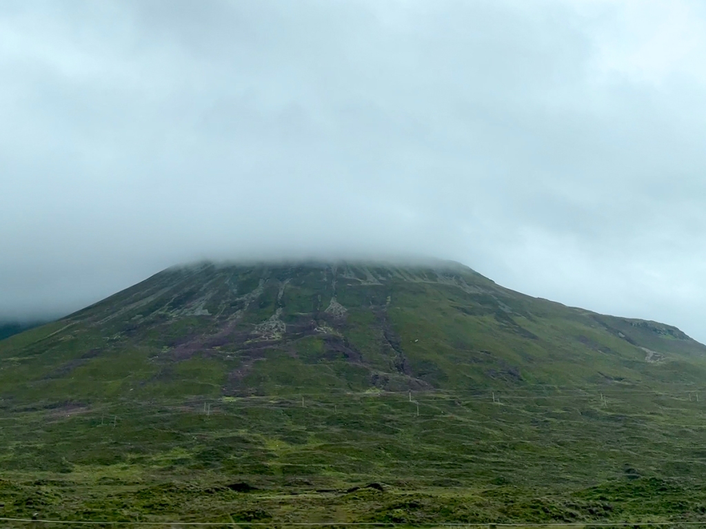 A green and dark purple mountain where the top is hidden by low cloud.